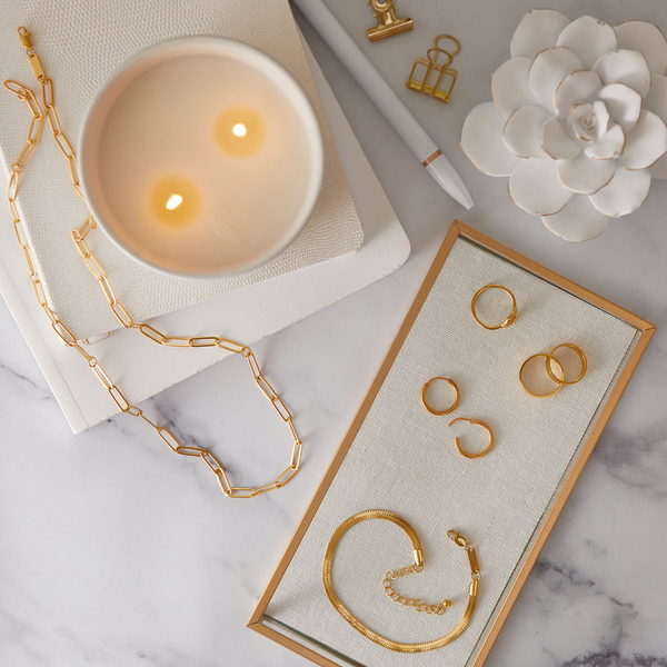 Des bijoux en plaqué or disposés sur des poses bijoux blanc, avec des teintes de dorées sur une table en marbre. 